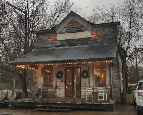 A rustic, weathered store with Coca-Cola signage, festive lights, and a porch adorned with wreaths.