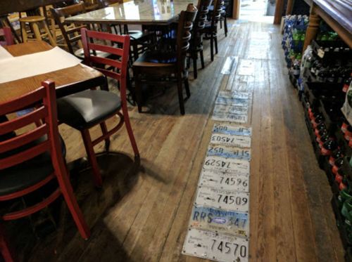 A wooden floor in a restaurant with a path made of various license plates and chairs in the background.