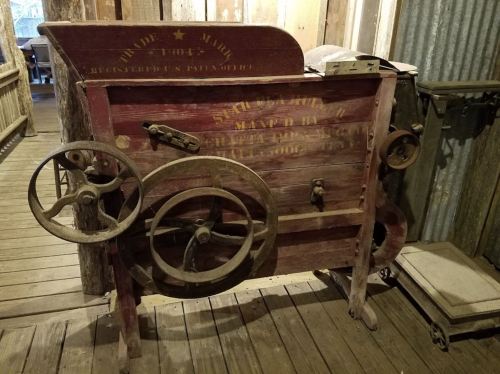An antique wooden machine with gears and wheels, displayed in a rustic setting.