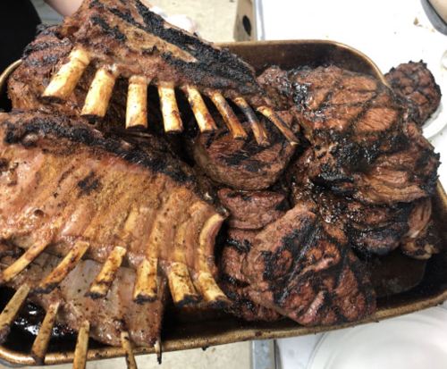 A tray of grilled meats, including ribs and steaks, with a charred, smoky appearance.