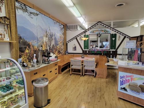 Cozy interior of a candy shop featuring a mountain mural, wooden furniture, and a display case of sweets.