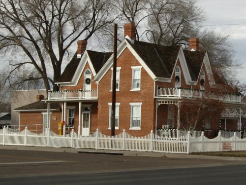 A historic two-story brick house with white trim and a picket fence, surrounded by bare trees under a cloudy sky.