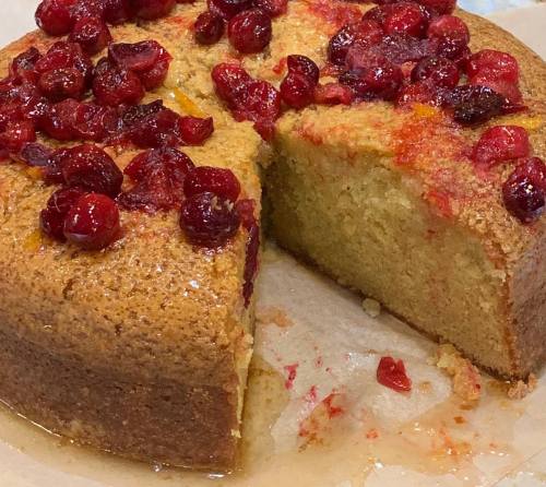 A round cake topped with red cranberries, partially sliced, resting on parchment paper.