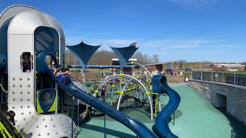 A colorful playground with slides and climbing structures under a clear blue sky, filled with children playing.