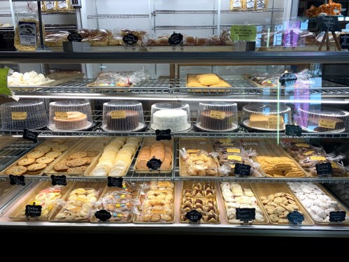 A display case filled with various baked goods, including cookies, pastries, and cakes, all labeled with price tags.