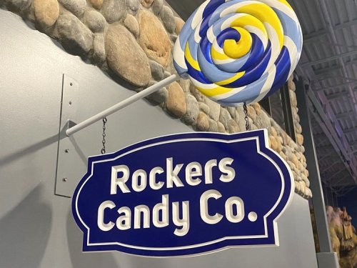 Sign for "Rockers Candy Co." with a colorful lollipop design, set against a stone wall background.
