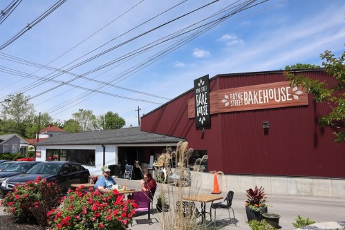 A red building with signs for "Payne Street Bakehouse" and "The Bake Lodge," featuring outdoor seating and blooming flowers.
