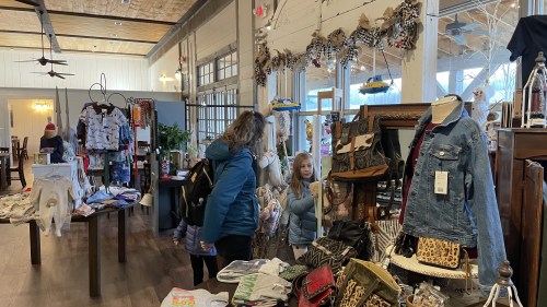 A cozy boutique with clothing displays; a woman and a child look at themselves in a mirror.