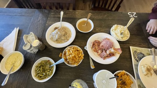 A table set with various dishes, including mashed potatoes, green beans, macaroni, ham, and gravy.