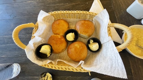 A basket of freshly baked rolls with butter in small containers, placed on a wooden table.