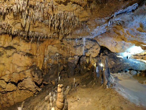 A dimly lit cave interior featuring stalactites hanging from the ceiling and stalagmites rising from the ground.