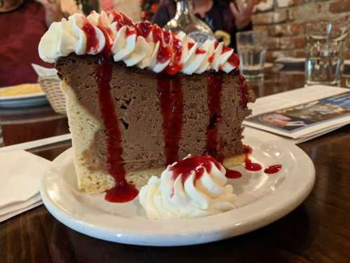 A slice of chocolate cheesecake topped with whipped cream and raspberry sauce, served on a white plate.