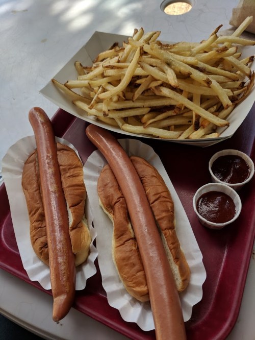 Two hot dogs in buns with a side of crispy French fries and two small cups of ketchup.