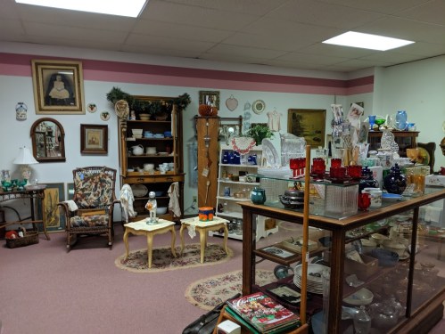 A cozy antique shop filled with vintage furniture, glassware, and decorative items on display.