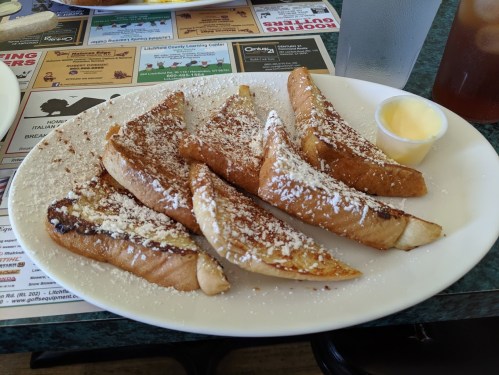 A plate of French toast slices dusted with powdered sugar, served with a small cup of butter.