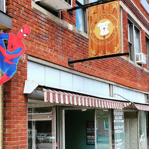 A Spider-Man figure is attached to a brick wall near a coffee shop sign that reads "Chubby Dog Coffee Co."
