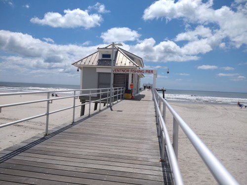 A wooden pier leads to a white building labeled "Ventnor Fishing Pier" with a sandy beach and ocean in the background.