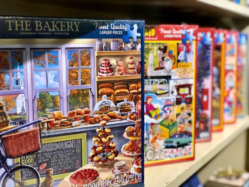 A colorful display of puzzle boxes featuring a bakery scene and various other themes on a shelf.