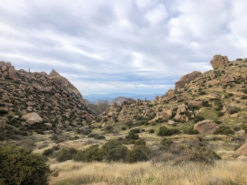 A rocky landscape with hills, sparse vegetation, and a cloudy sky in the background.