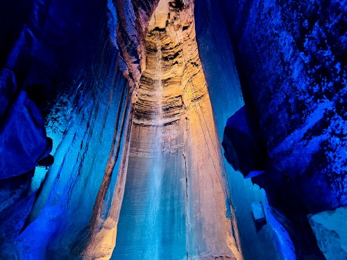 A stunning cave interior with illuminated blue and orange walls, featuring a waterfall cascading down the rocky surface.