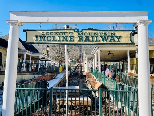 Sign for Lookout Mountain Incline Railway with tracks and visitors in the background on a clear day.