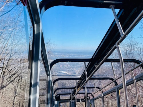 View from inside a cable car, showcasing a clear blue sky and distant landscape through the glass roof.