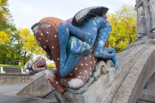 Colorful abstract sculpture featuring intertwined figures with polka dots, set in a park with greenery in the background.