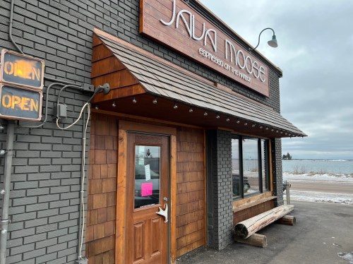 Exterior of Java Moose café with a wooden door, sign reading "OPEN," and a snowy landscape in the background.