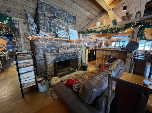 Cozy rustic interior of a cabin with a stone fireplace, wooden bar, and festive decorations.