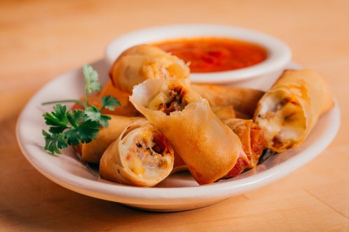 A plate of crispy spring rolls with a side of dipping sauce and a sprig of cilantro.