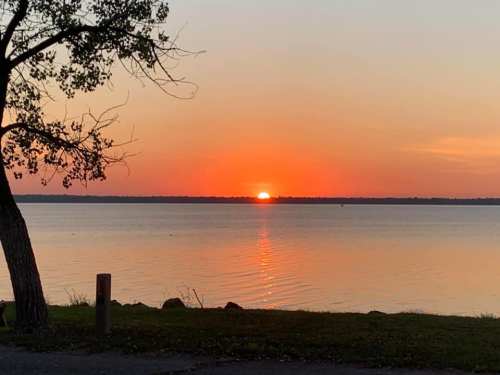 A serene sunset over a calm lake, with vibrant orange and pink hues reflecting on the water's surface.