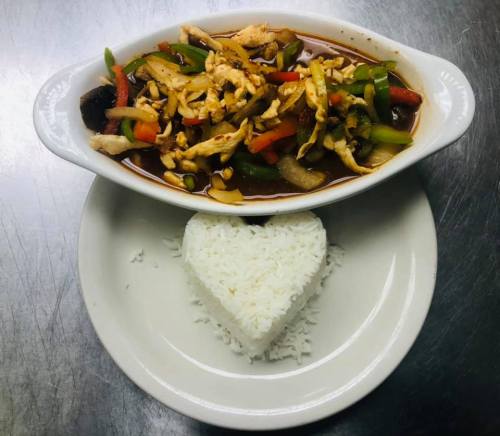 A dish of stir-fried vegetables and chicken in sauce, served with heart-shaped white rice on a plate.
