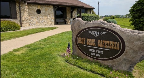 Sign for Gray Bros. Cafeteria, a family-owned restaurant since 1954, with a stone exterior and landscaped surroundings.