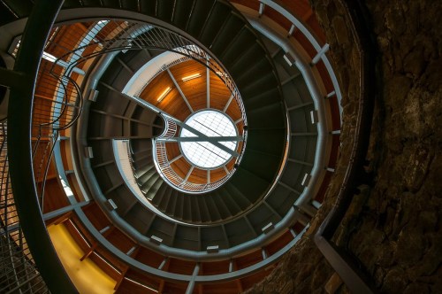 A spiral staircase viewed from below, featuring wooden and metal elements with a circular skylight above.