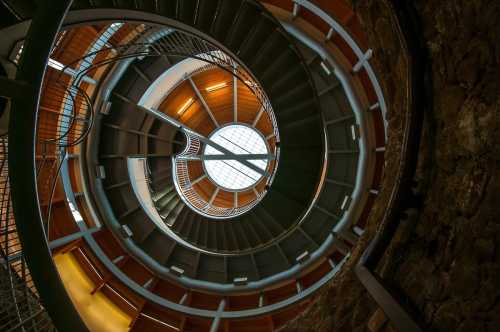 A spiral staircase viewed from below, featuring wooden and metal elements with a circular skylight above.