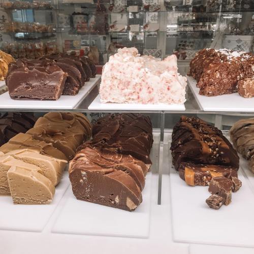 A display of various fudge flavors, including chocolate, peanut butter, and peppermint, arranged on white trays.