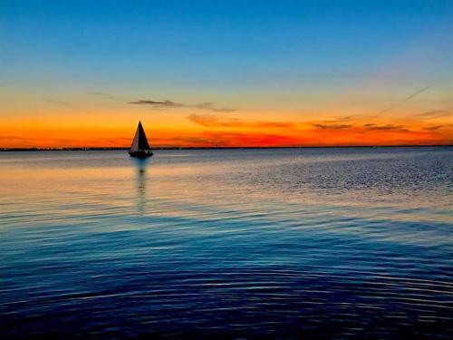 A sailboat glides across calm waters at sunset, with vibrant orange and blue hues in the sky.