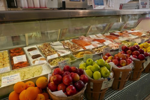 A display of fresh seafood and colorful fruits in baskets at a market, with labels for various items.