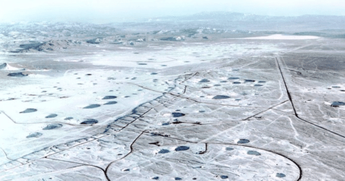 Aerial view of a vast, barren landscape with numerous circular depressions and sparse vegetation.