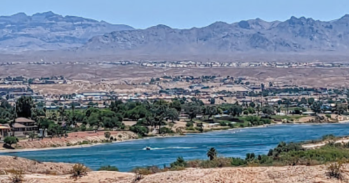 A scenic view of a river surrounded by mountains and desert landscape under a clear blue sky.
