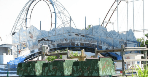 A partially constructed roller coaster with a blue and white design, surrounded by green planters and fencing.