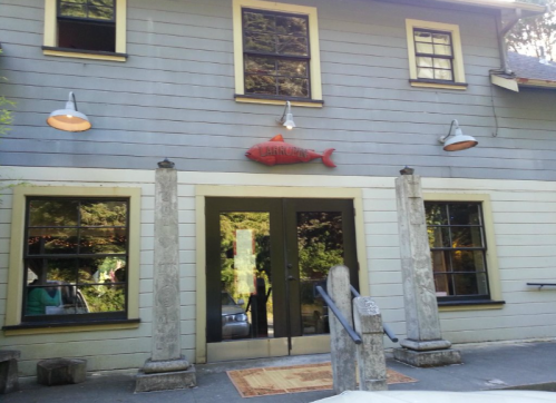 A rustic building with gray siding, large windows, and a red fish sign above the entrance.