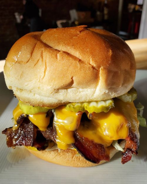 A close-up of a cheeseburger with melted cheese, pickles, and lettuce on a soft bun.