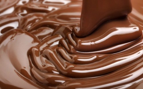Close-up of smooth, melted chocolate with a hand gently stirring it, creating ripples in the rich, glossy texture.