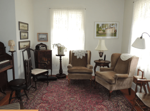 Cozy living room with two armchairs, a small table, and vintage decor, illuminated by natural light through sheer curtains.