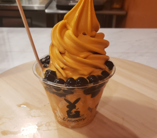 A cup of orange soft serve ice cream topped with black tapioca pearls, served with a wooden stick.