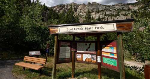 Sign for Lost Creek State Park with a wooden bench and mountainous landscape in the background.