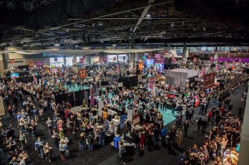 A large crowd gathers in a spacious convention center filled with booths and displays.
