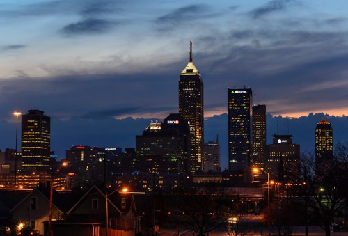 City skyline at dusk with illuminated buildings and a dramatic sky in the background.