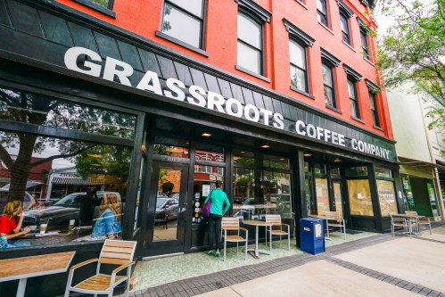 Exterior of Grassroots Coffee Company, featuring large windows, outdoor seating, and a vibrant red building.